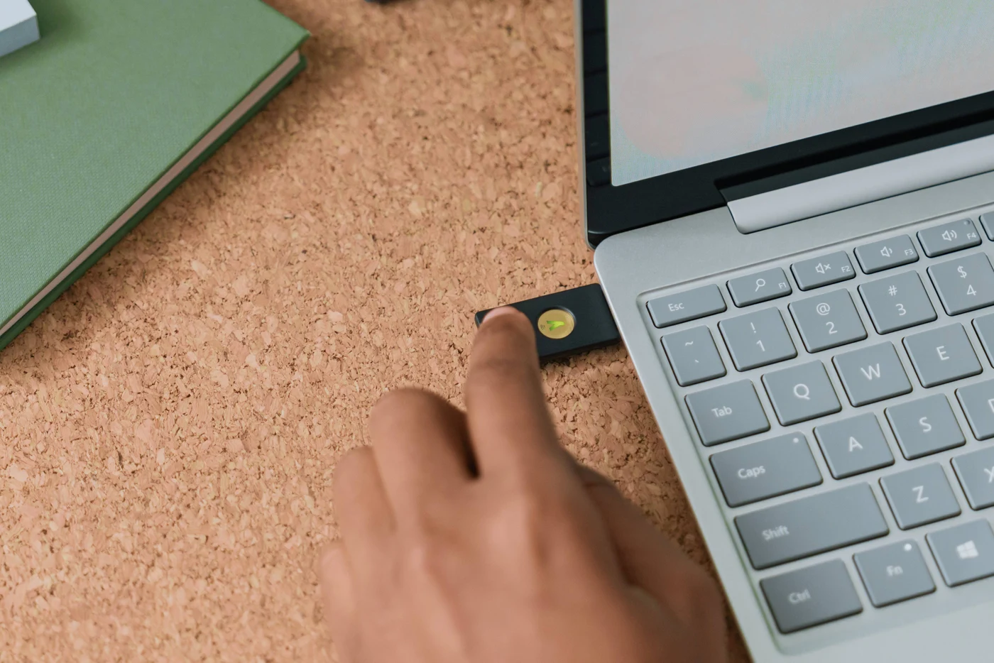Prst dodiruje YubiKey umetnut u bočni priključak prijenosnika na plutenom stolu